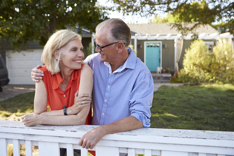 Older couple leaning over backyard fence.