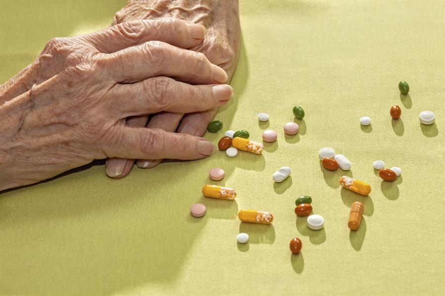 Arthritic hands beside an assortment of pills.