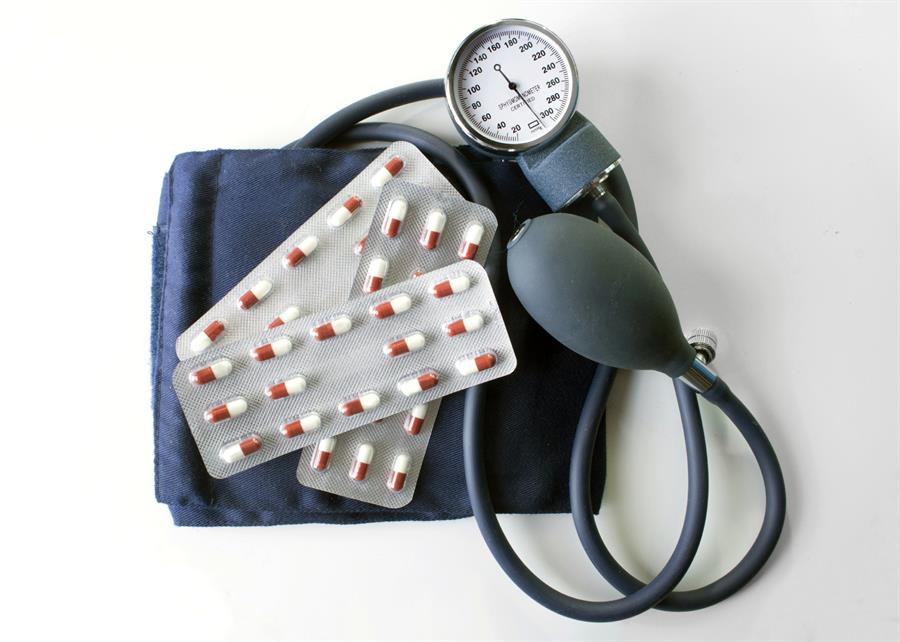 Blood pressure cuff wrapped around blister pack of red and white pills.