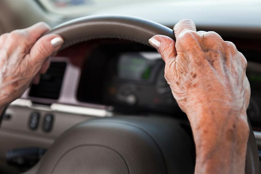 Close up of an older womans hands holding a car steering wheel.