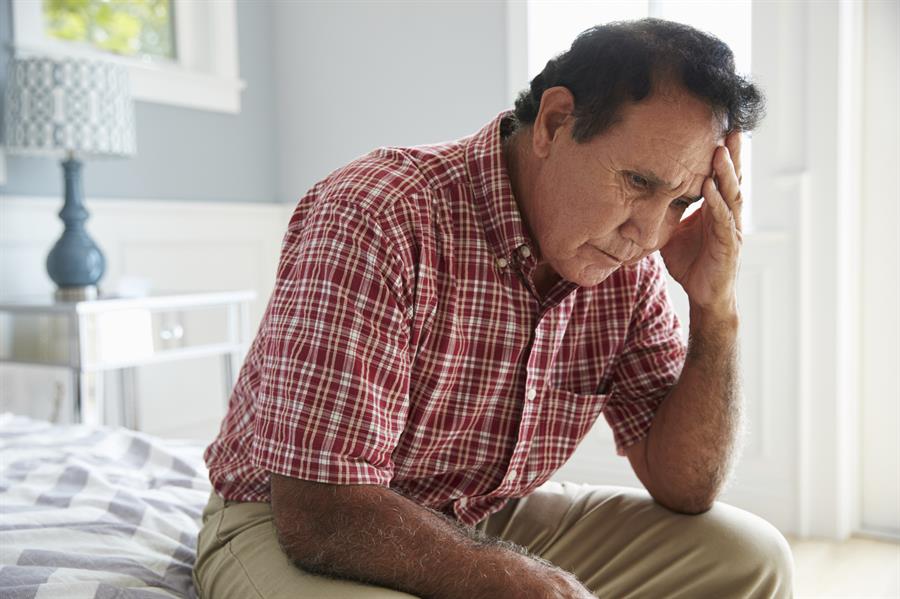 Man sitting on a bed with his head in one of his hands.