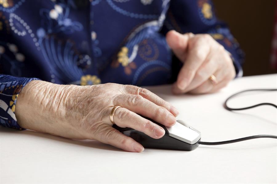 Older person's hand with wedding ring resting on computer mouse.