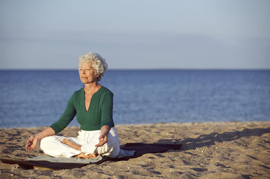 Older woman doing yoga on the beach.