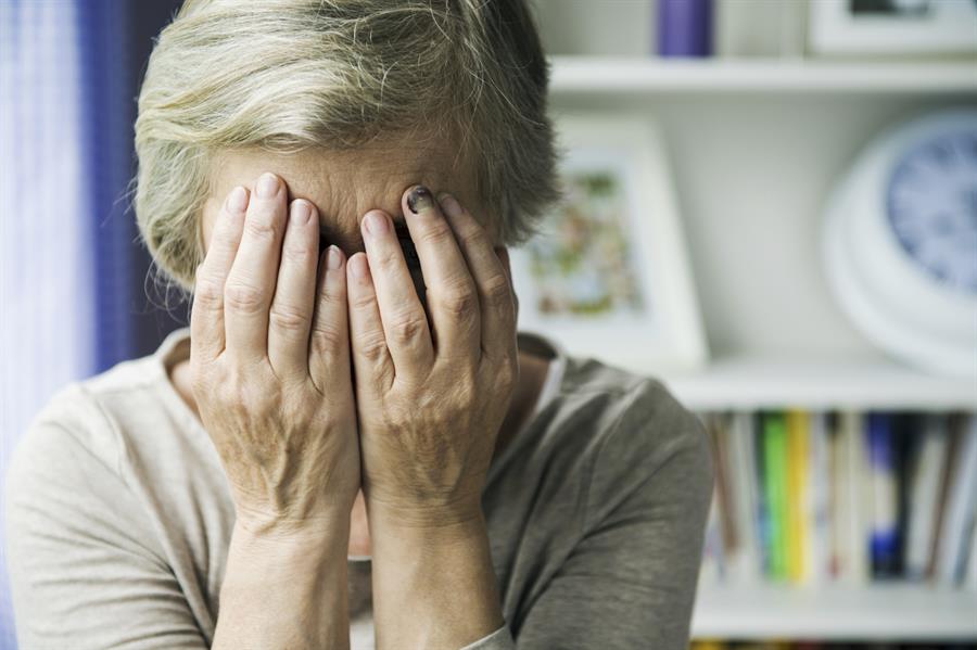 Senior woman holding hands over face with a bruised middle fingernail.