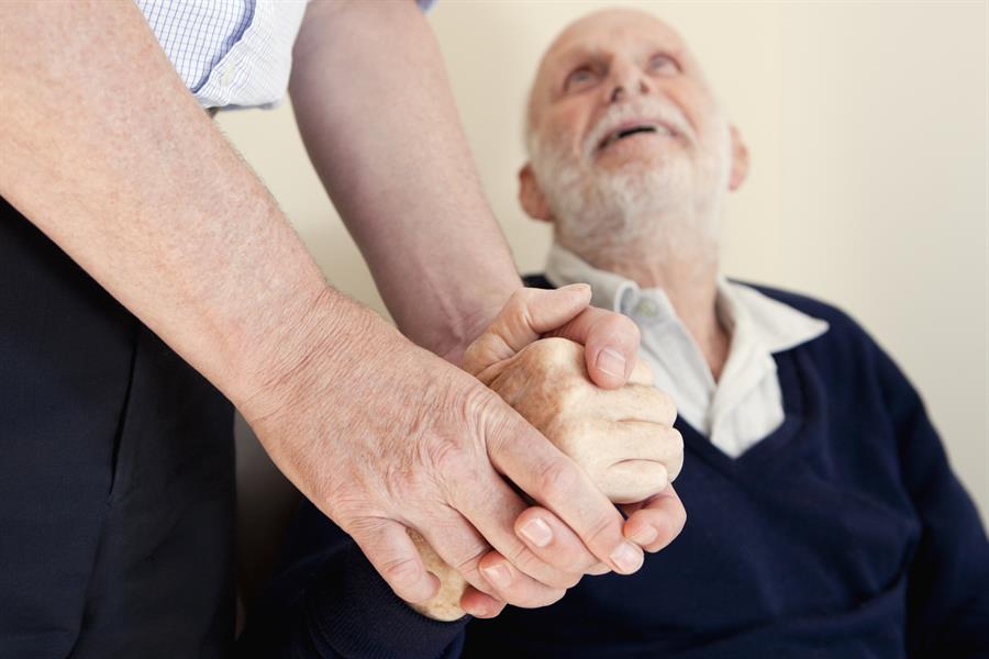 Elderly man looking up at the person he is holding hands with.