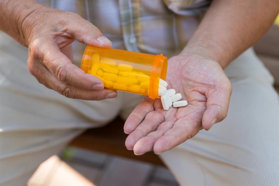 Older man's hands tipping pills out of a prescription bottle