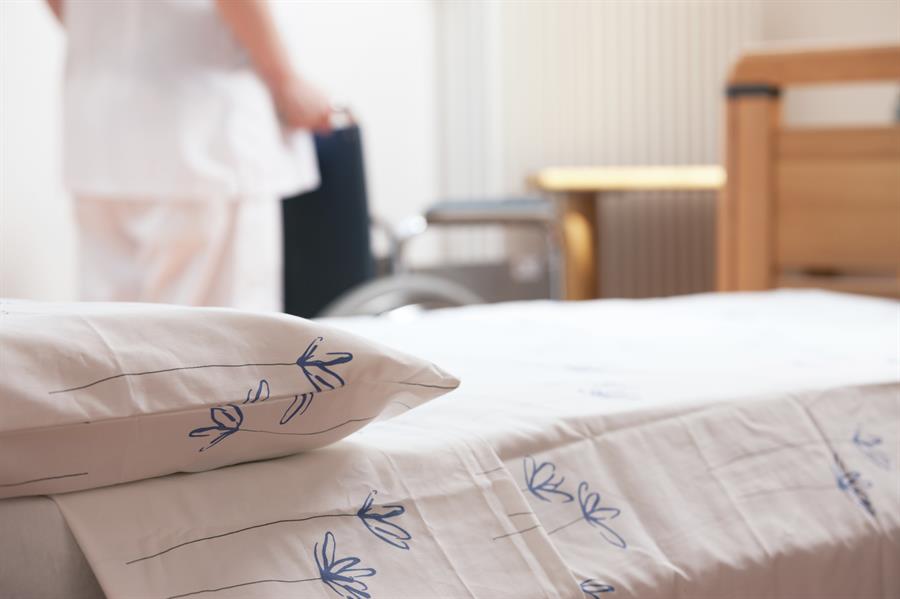 Close-up of hospital bed with wheelchair in background.