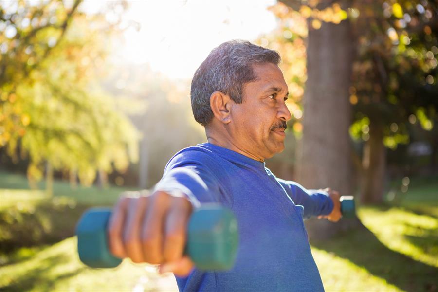 Older man outdoors arms outstretched lifting weights.