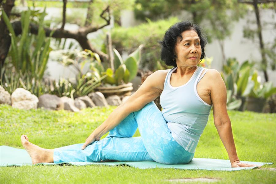 Older woman on grass stretching in yoga pose.