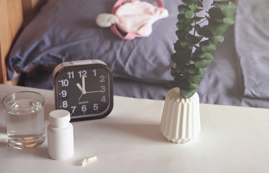 Pills, glass of water and alarm clock on a bed side table