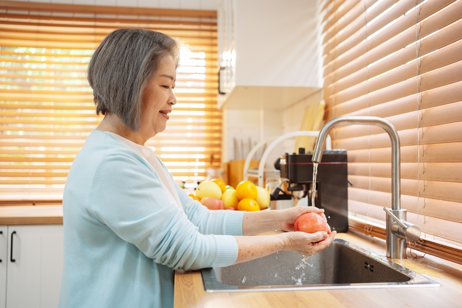 Older adult woman washing fruit in a kitchen.