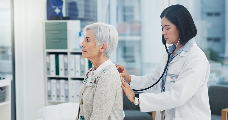 Patient sitting in a doctor's office while the doctor uses a stethoscope on their back to check their breathing.