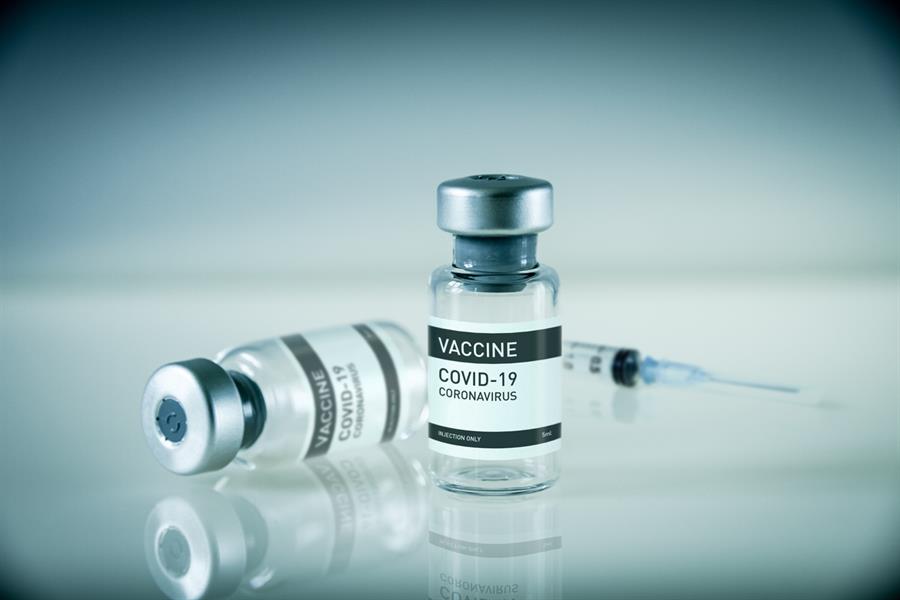 Covid-19 vaccine bottle and syringe on a blue laboratory background.