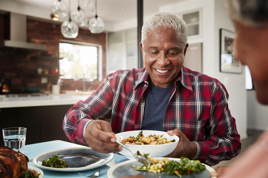 Older adult male having a meal in the kitchen and putting food onto a plate. 