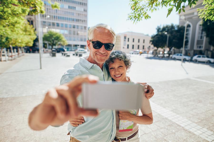 Smiling couple taking a selfie on a mobile phone on a sunny day outdoors.