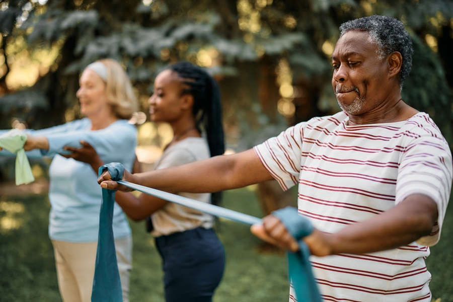 Two older adults using resistance bands outside with the supervision of a trainer.