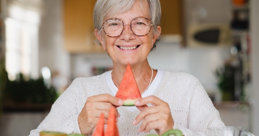 Elderly woman sitting down and smiling with a slice of watermelon in her hands.