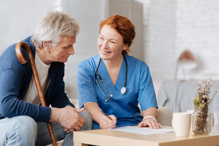 Smiling nurse sitting down while explaining documents to an elderly man.