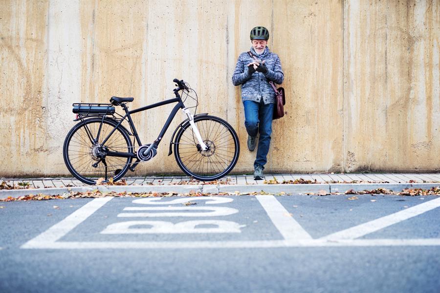 Active senior man leaning against a concrete wall and using a smartphone with his bike next to him.