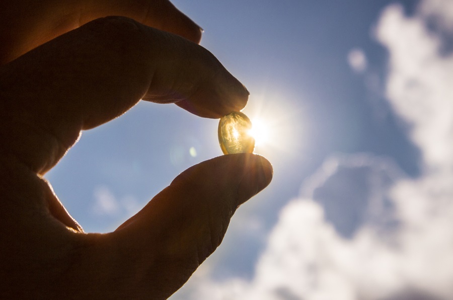 Human hand holding vitamin D capsule with sun in the background