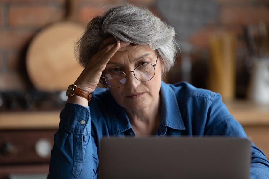 Mature woman looking at laptop screen in her home and feeling tired and confused.