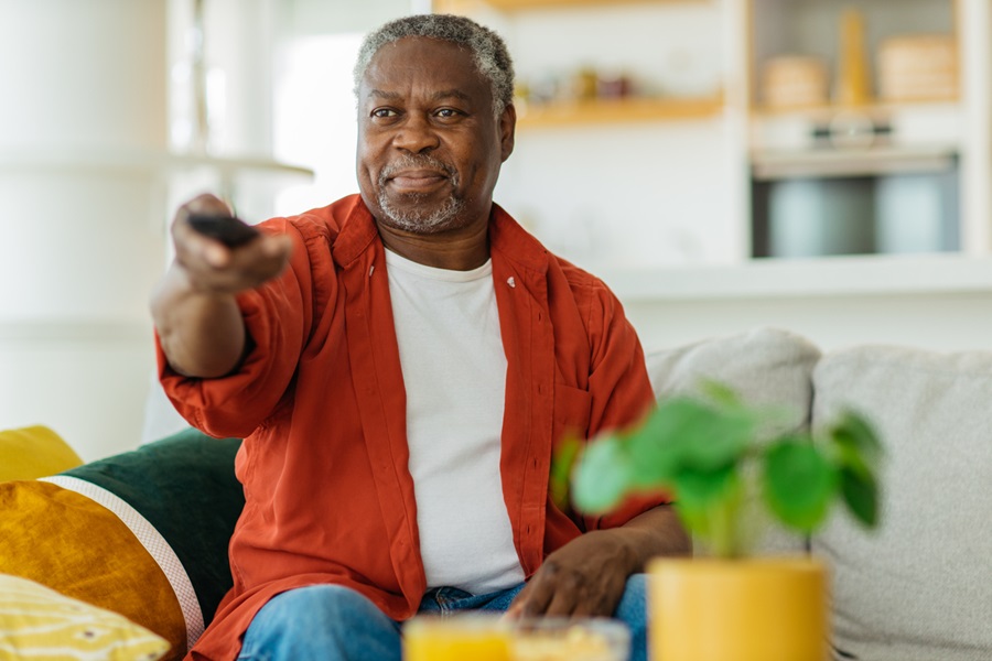 Senior man sitting in his home holding a remote control and watching TV.