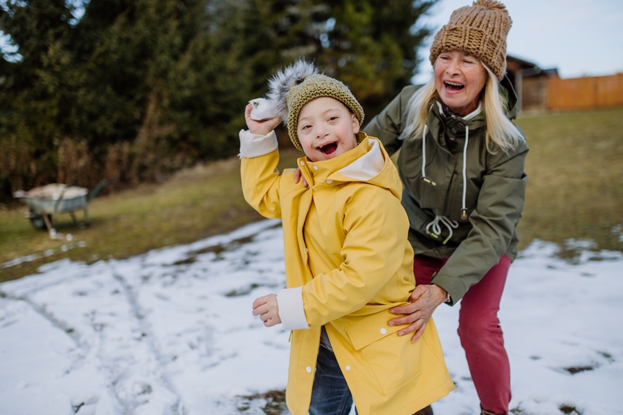 A disabled child playing in the snow with their grandparent.