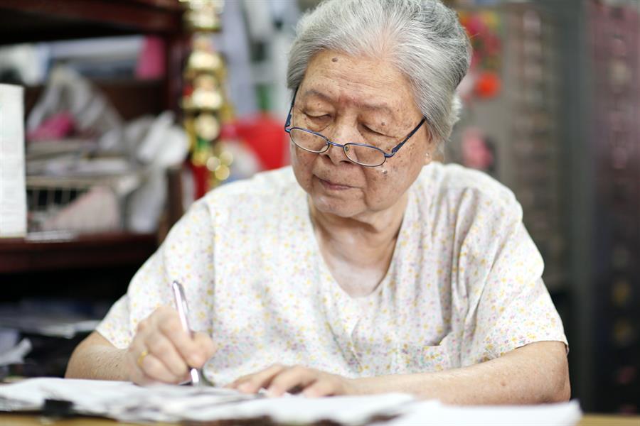 Focused senior woman wearing glasses sitting and writing in a notebook.