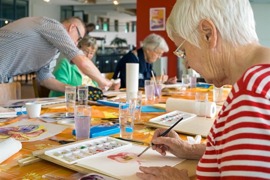 Woman working on watercolor painting at table with other students.