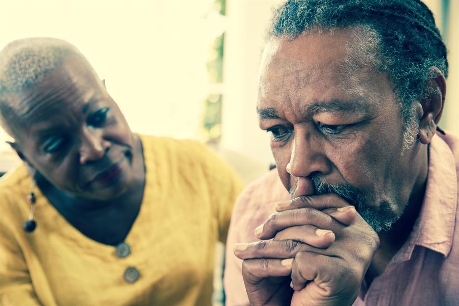 A senior woman comforting a worried man with his fingers interlocked.