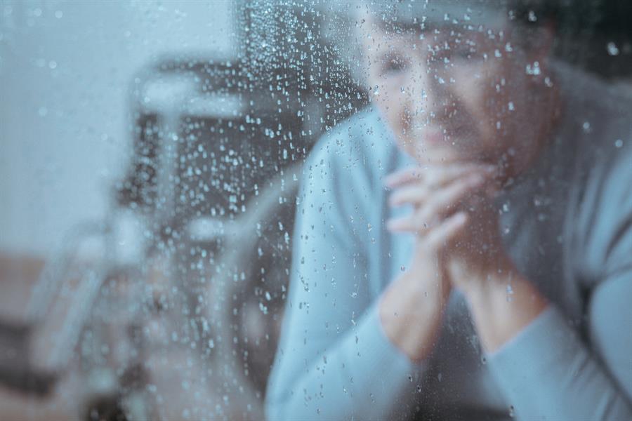 Depressed older woman looking through a rainy windowpane.