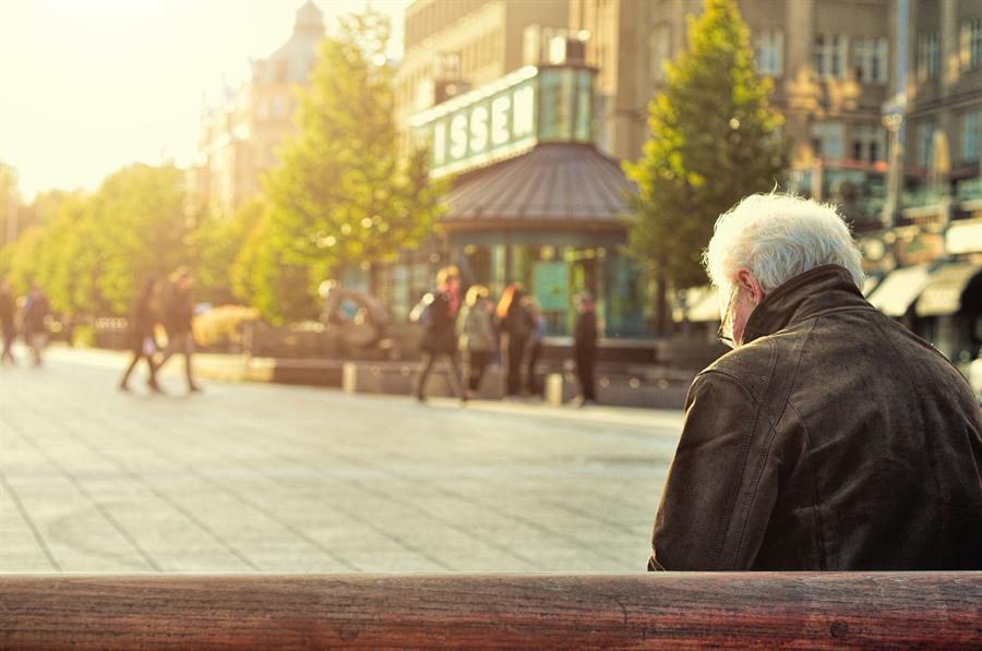 Senior man looking down and sitting on a bench alone on a sunny afternoon.