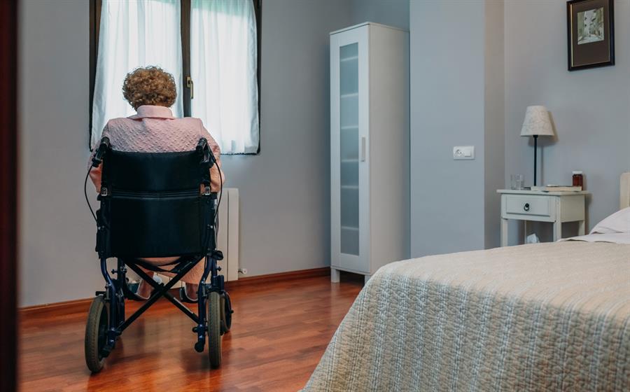 Senior woman in wheelchair looking outside of her bedroom window.