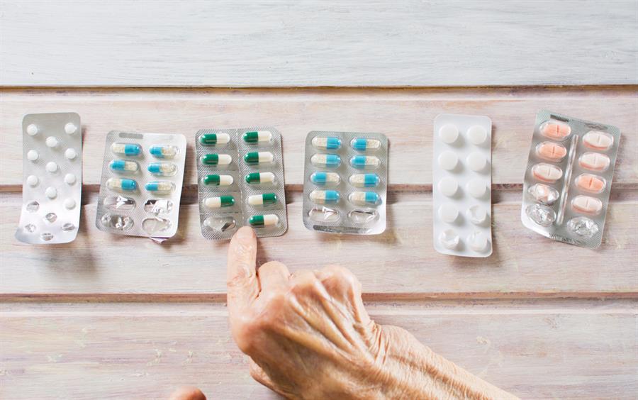 Older adult choosing from a line-up of medications placed on a wooden table. 