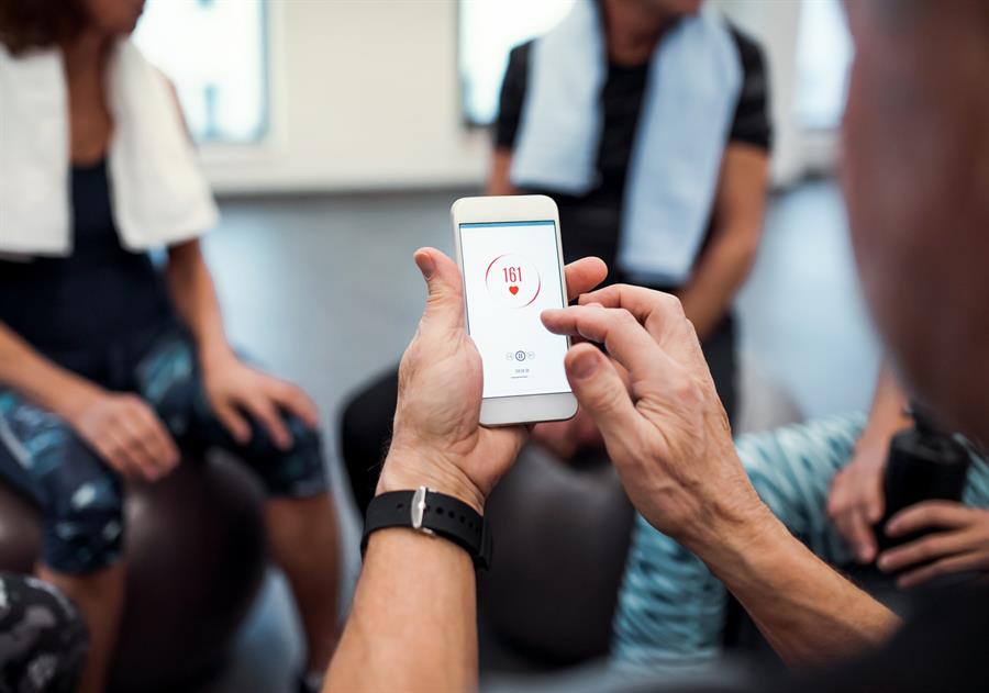 Group of people sitting on exercise balls. One man is holding a smartphone with a health application open on the screen.