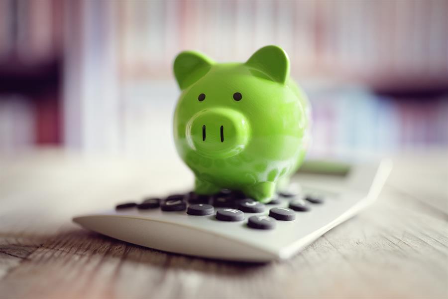 A green piggybank sitting on top of a calculator.