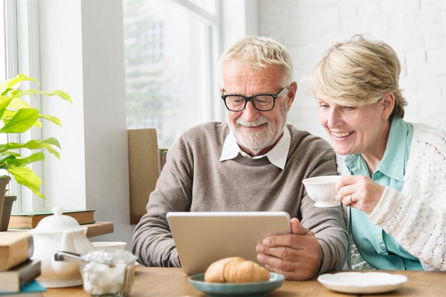 Senior couple reading on an etablet at the breakfast table.