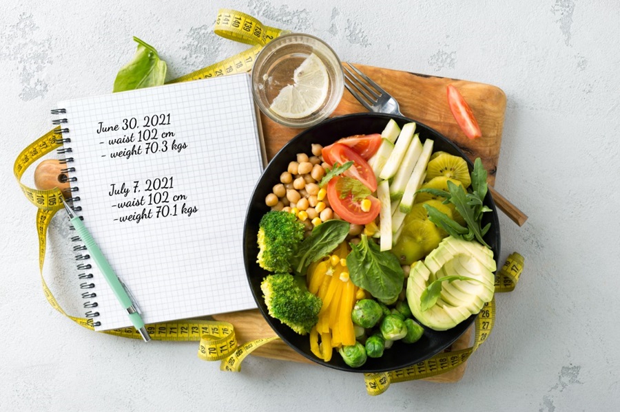 Vegetarian buddha bowl with blank notebook and a measuring tape to depict healthy diet for weightloss