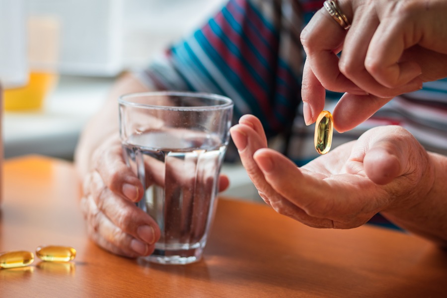 Someone sitting down at a table with a glass of water in one hand and accepting a vitamin tablet in the other hand.